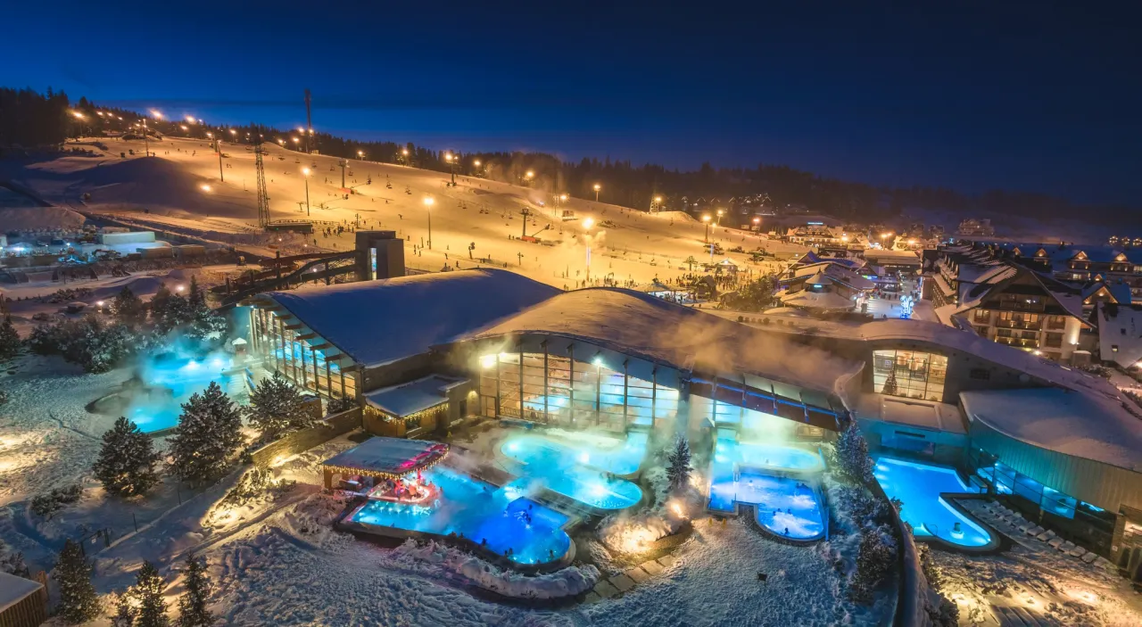 Oświetlone baseny termalne w śnieżną noc, obok stoku narciarskiego. Idealne miejsce, by sprawdzić, które termy w Polsce są najlepsze.