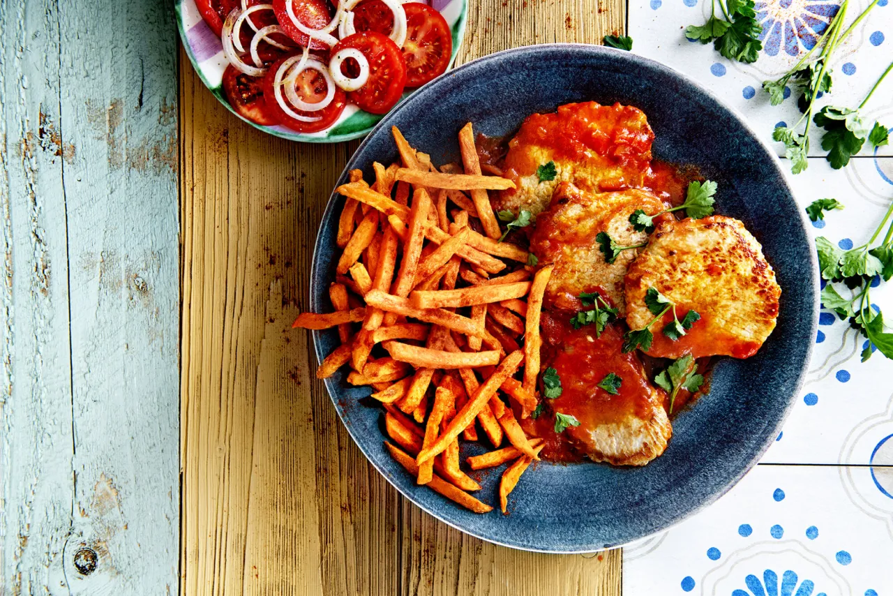 Mięso w sosie pomidorowym z porcją frytek na szybko. Obok sałatka z pomidor&oacute;w i cebuli.