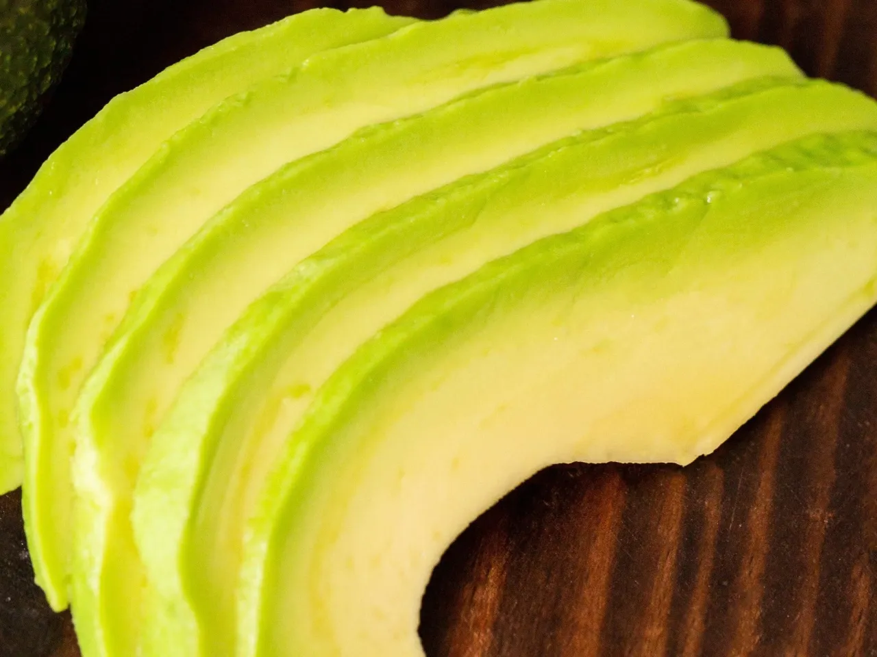 Plasterki awokado na ciemnym tle. Ten owoc jest bogaty w zdrowe tłuszcze, kt&oacute;re mogą pom&oacute;c w obniżeniu poziomu cholesterolu.