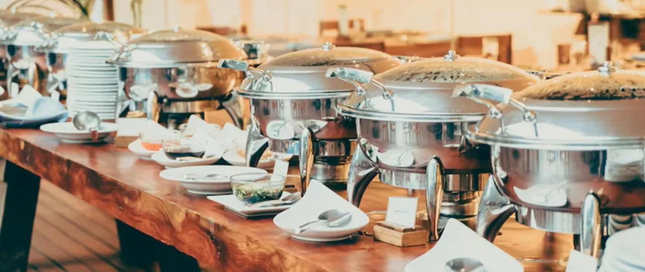St&oacute;ł z podgrzewaczami do jedzenia, talerzami i sosami. Idealne wyposażenie, gdy zastanawiasz się, jak założyć firmę cateringową w domu.