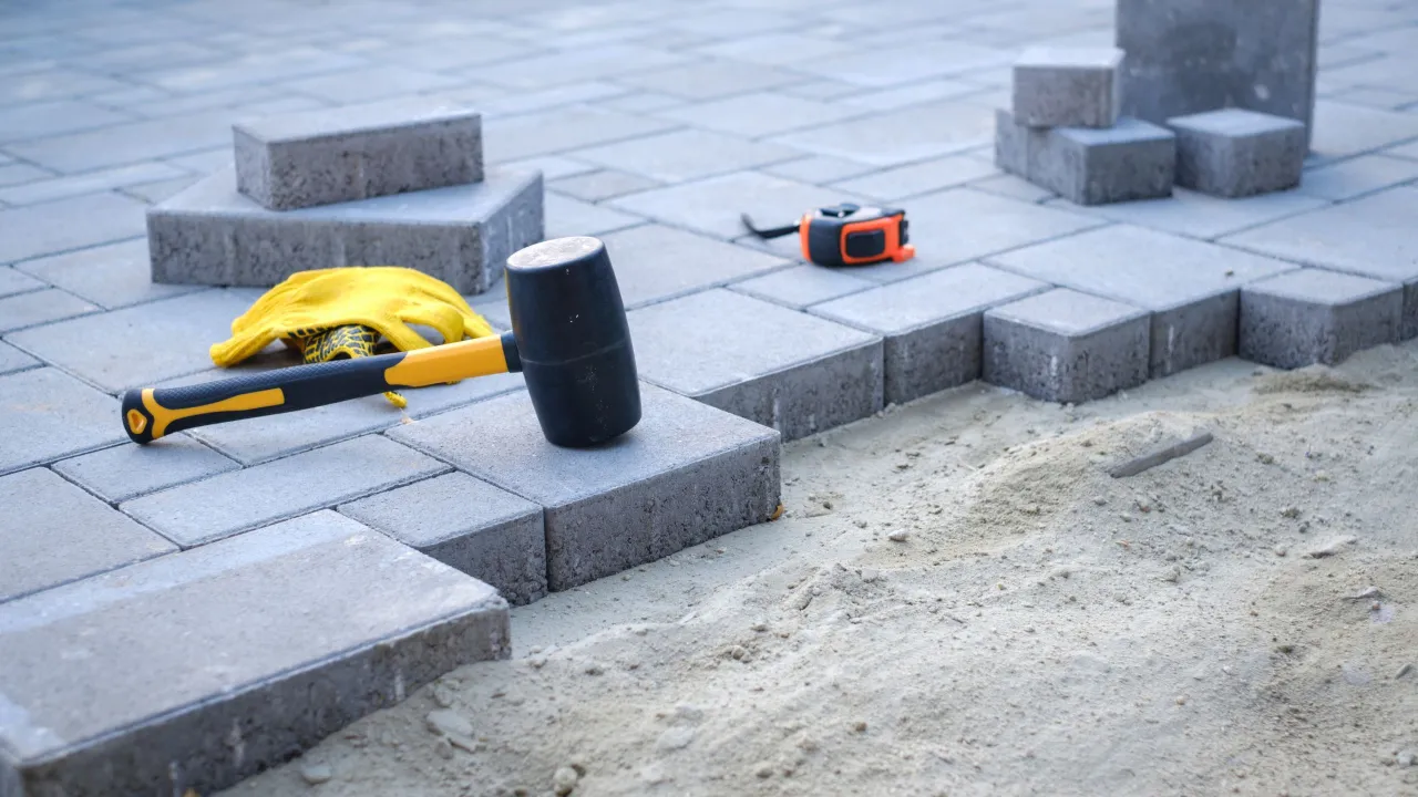 Praca nad podjazdem: gumowy młotek, rękawice i miarka leżą na suchym betonie pod kostkę.