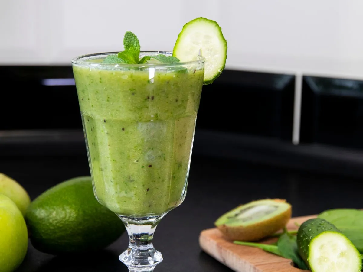 Zielony koktajl z miętą i plasterkiem og&oacute;rka, obok jabłka, limonki i kiwi. Idealny na zdrowe koktajle sirt przepisy.