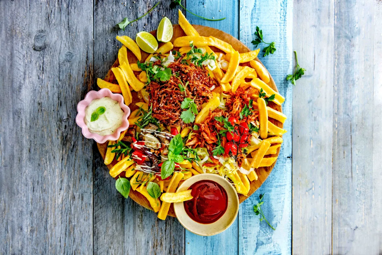 Talerz pełen chrupiących frytek z szarpanym mięsem, pomidorkami koktajlowymi, ziołami i dipami. Idealne frytki z czymś pysznym!