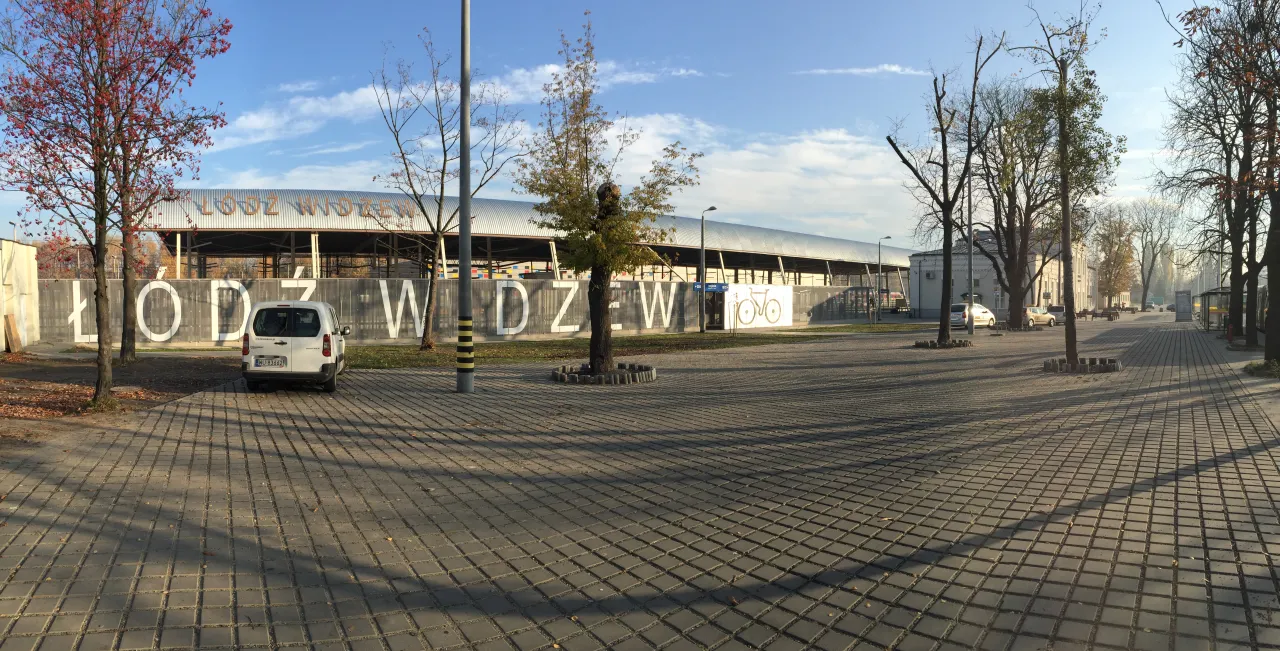 Łódź Widzew: biały bus i drzewa na tle nowoczesnego dworca PKP.