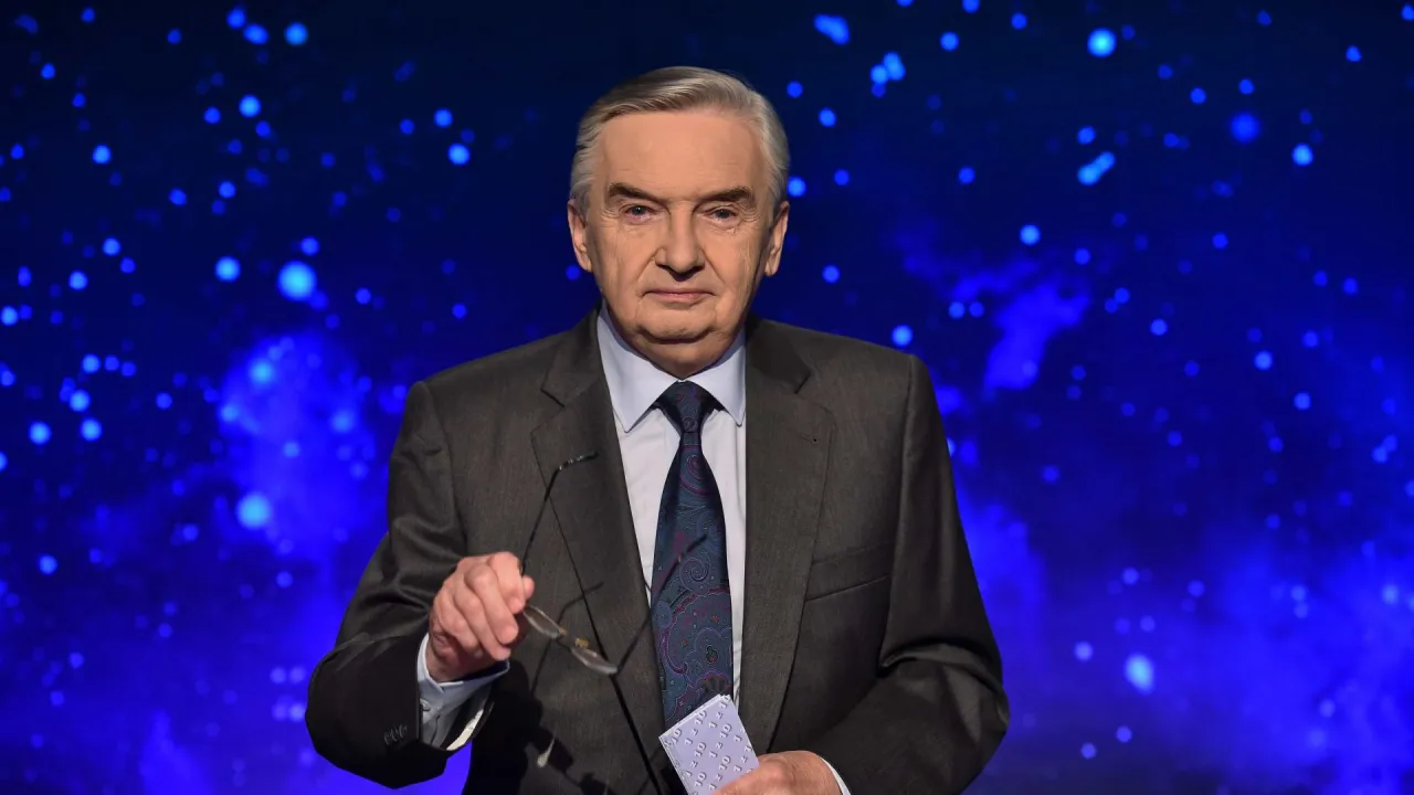 Starsza elegancka osoba w garniturze, trzymająca okulary i kartkę z napisem 