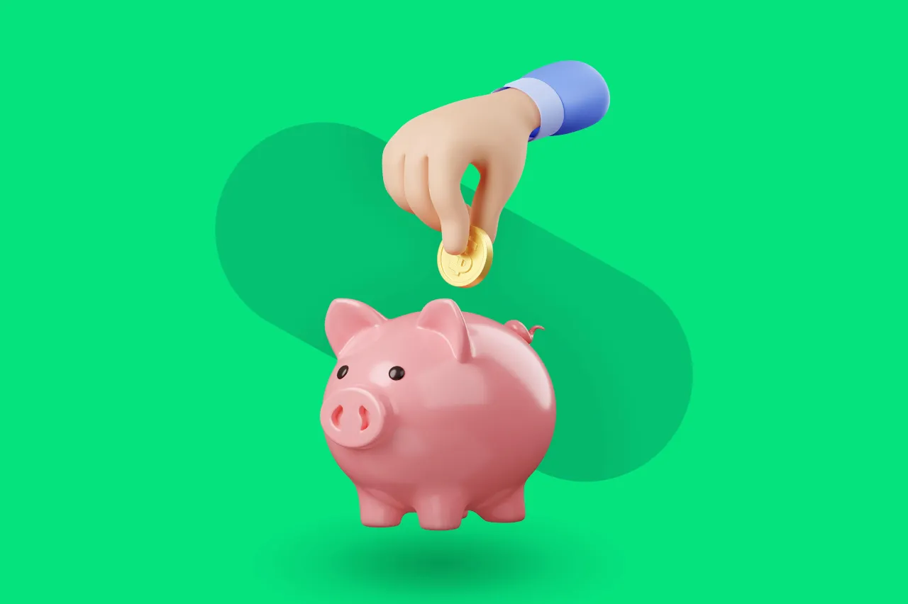 R&oacute;żowa świnka skarbonka, do kt&oacute;rej ręka wrzuca monetę. Idealny obrazek na blog o tym, jak oszczędzać pieniądze.