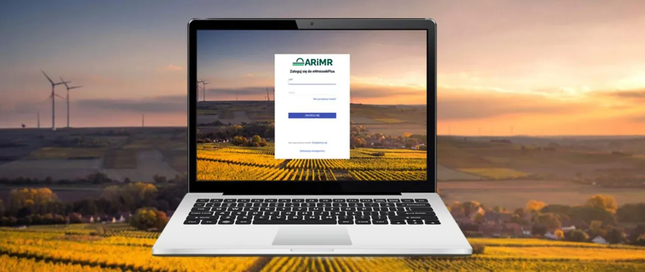 Laptop z widokiem na pola i wiatraki, na ekranie logowanie do systemu ARiMR. Sprawdź, jak sprawdzić wysokość dopłat bezpośrednich.