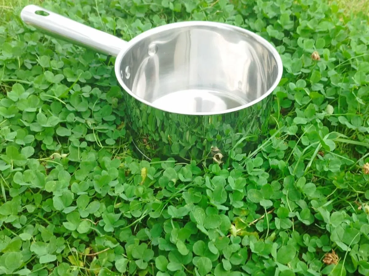 Stalowy garnek z długą rączką stoi na zielonej trawie. Może służyć jako nietypowe garnki do jakich śmieci, gdyby tylko ktoś chciał.