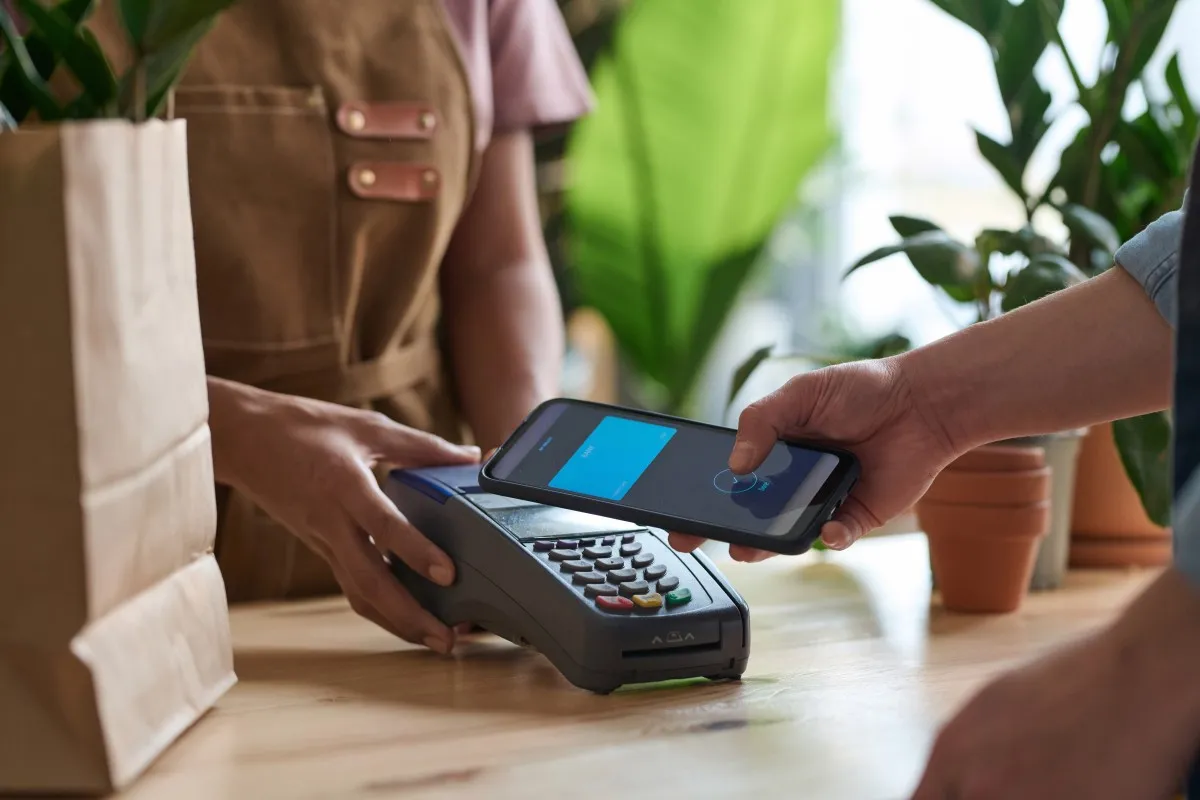 Klient płaci telefonem w sklepie, zbliżając smartfon do terminala. To prosty sposób, jak płacić telefonem Millenium.