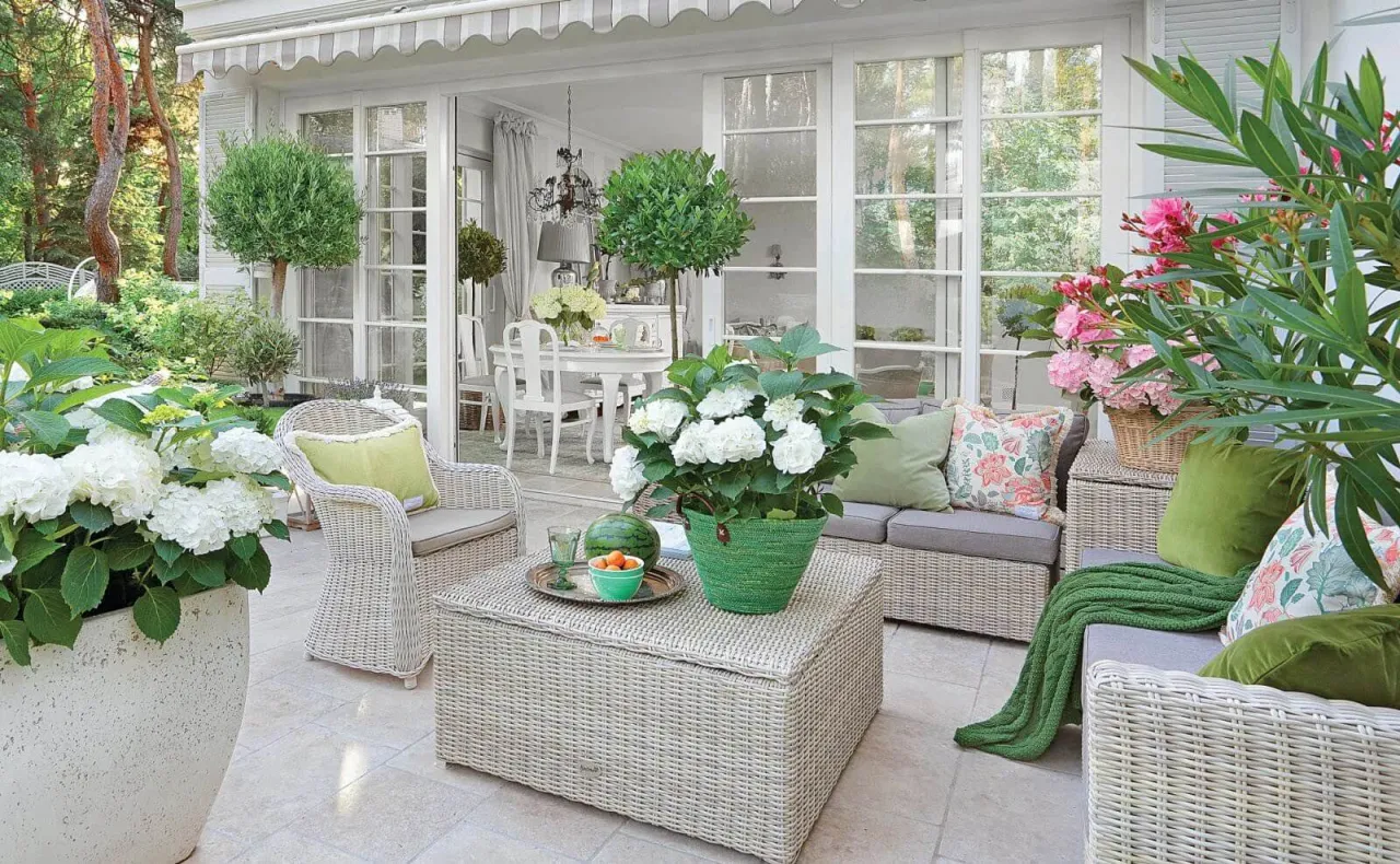Białe hortensje na tarasie tworzą letnią oazę. Wygodne meble rattanowe i zieleń roślin zapraszają do relaksu.