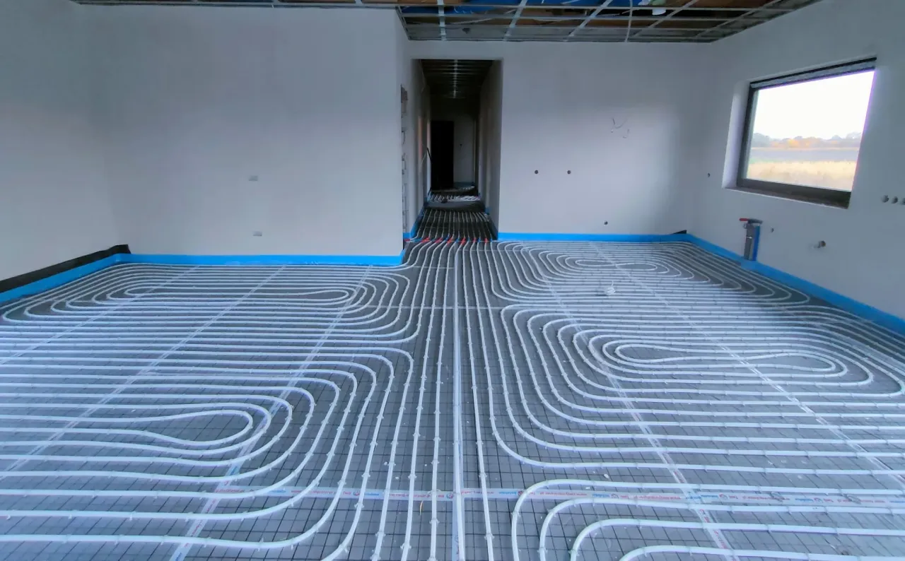 Instalacja ogrzewania podłogowego w nowym domu. Rury tworzą skomplikowany wz&oacute;r, gotowe do zalania betonem. To przyszłość komfortu cieplnego, alternatywa dla tradycyjnych grzejnik&oacute;w.