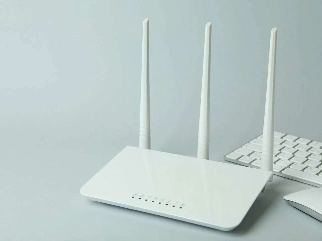 Biały router Wi-Fi z trzema antenami, obok klawiatury i myszki. Idealny do szybkiego internetu ac l ac n.