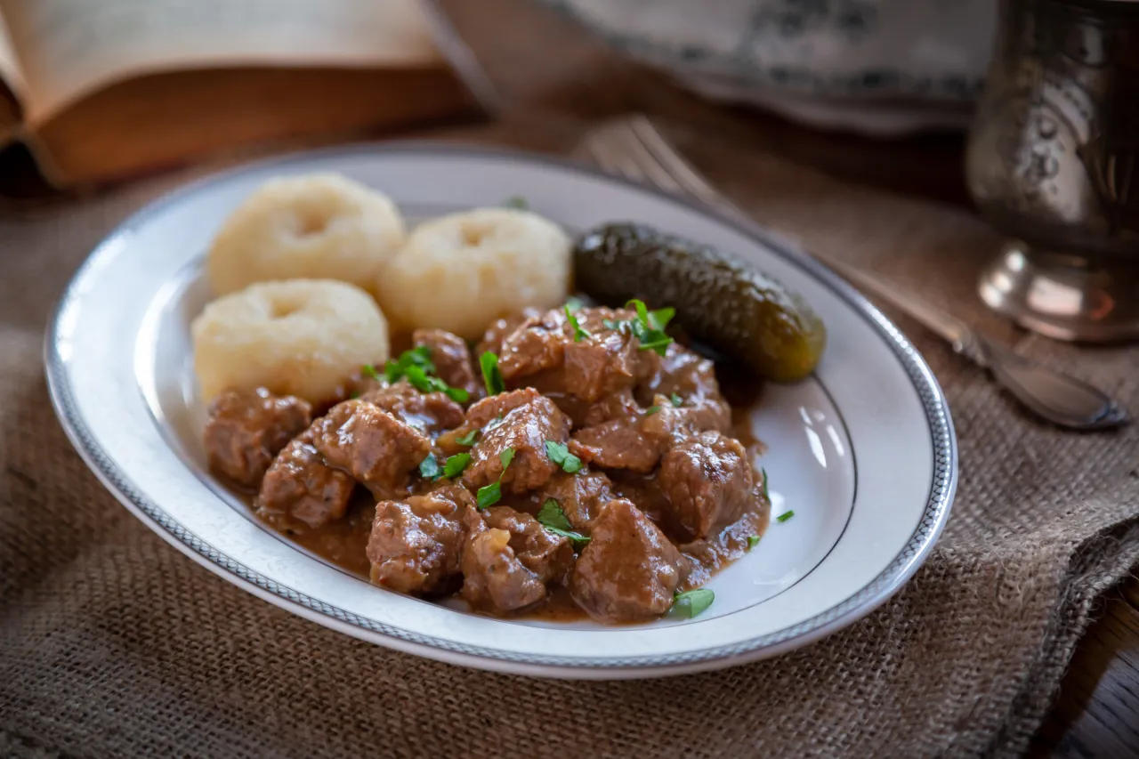 Pyszny gulasz z wołowiny z kluskami śląskimi i og&oacute;rkiem kiszonym, posypany natką pietruszki.