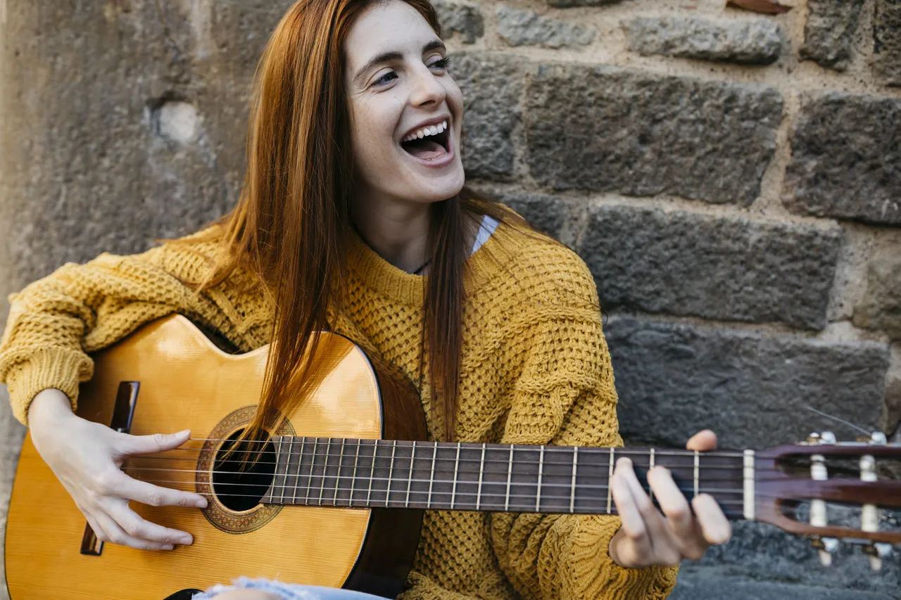 osoba grająca na gitarze akustycznej, uśmiechnięta