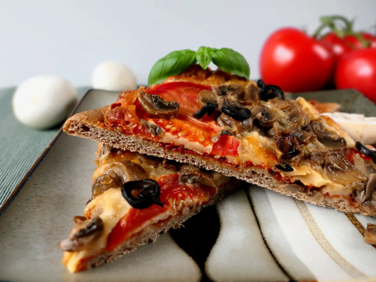 Dwie kromki pizzy z pieczarkami, oliwkami i pomidorami. Wegański ser z czego? Z pewnością z roślinnych składnik&oacute;w, pyszny!