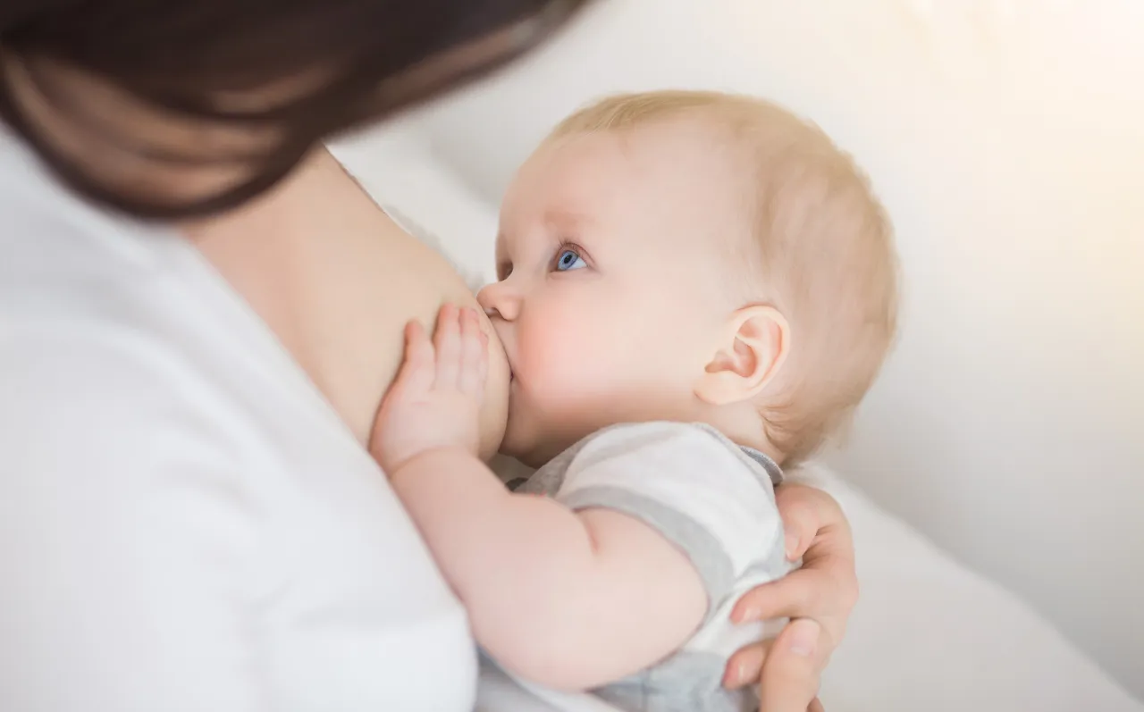 mama karmiąca piersią z dzieckiem, lekko przeziębiona, uśmiechnięta