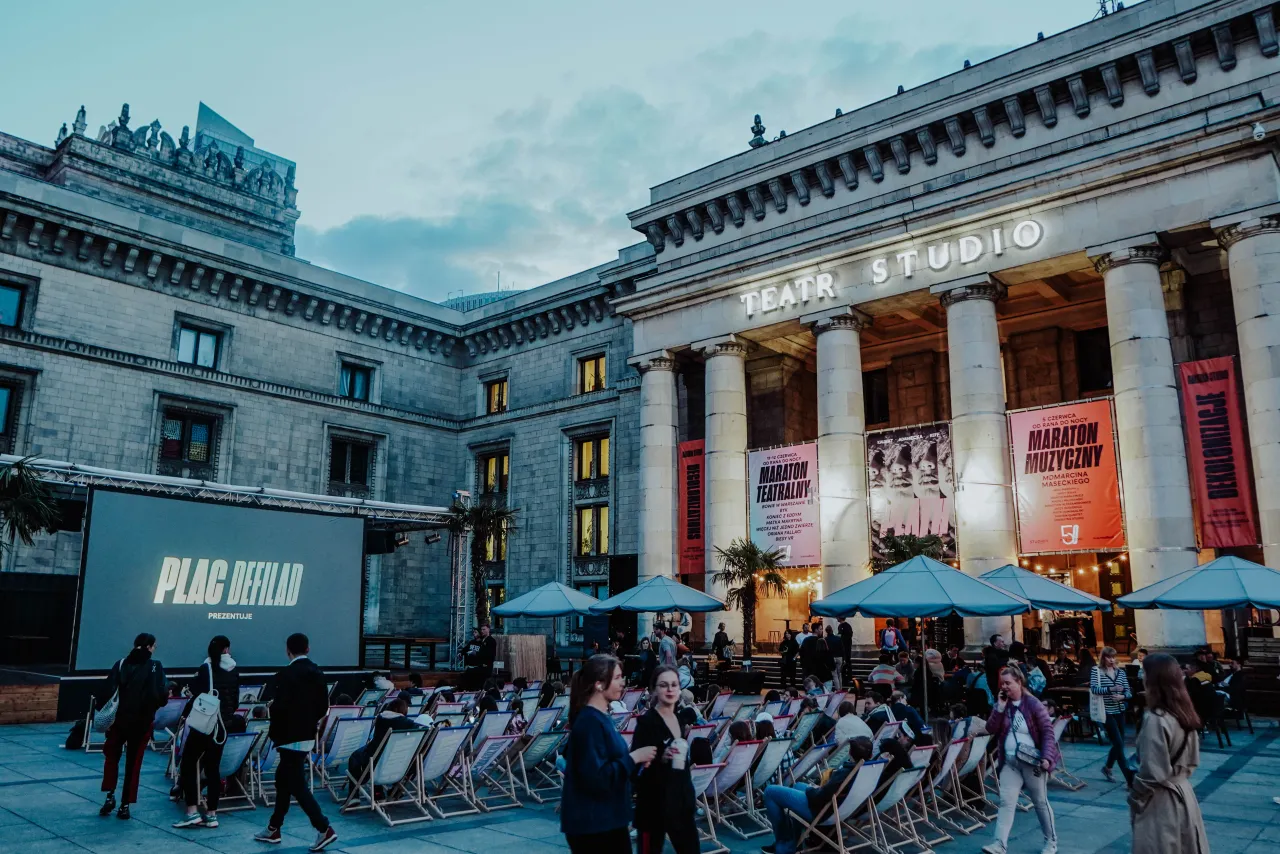 Plac Defilad przed Teatrem Studio w Warszawie. Ludzie siedzą na leżakach, czekając na wydarzenie.