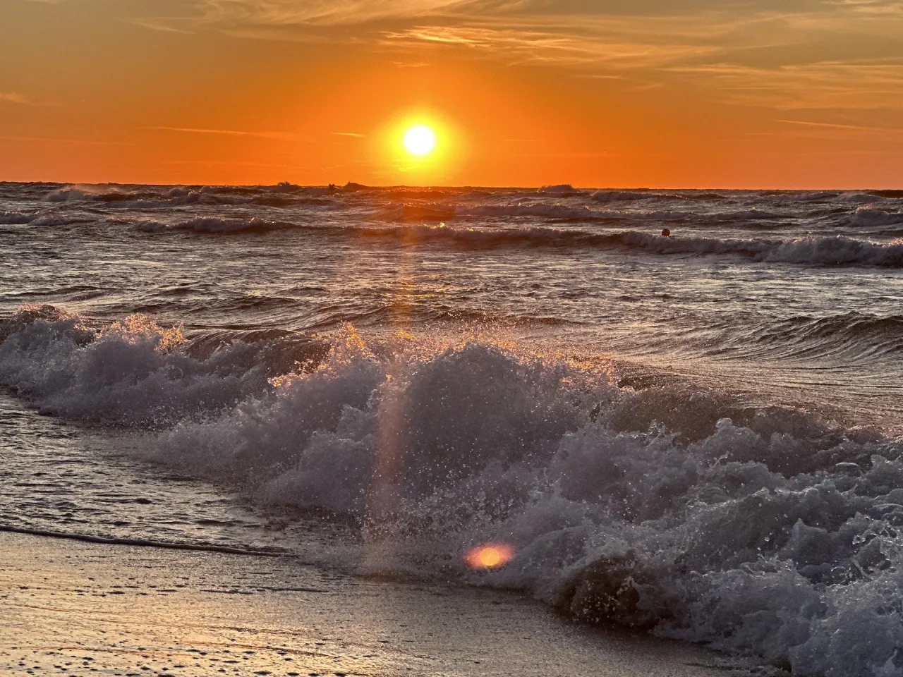 Zach&oacute;d słońca nad Bałtykiem, jedna z najpiękniejszych miejsc nad polskim morzem. Fale rozbijają się o brzeg, tworząc pianę.