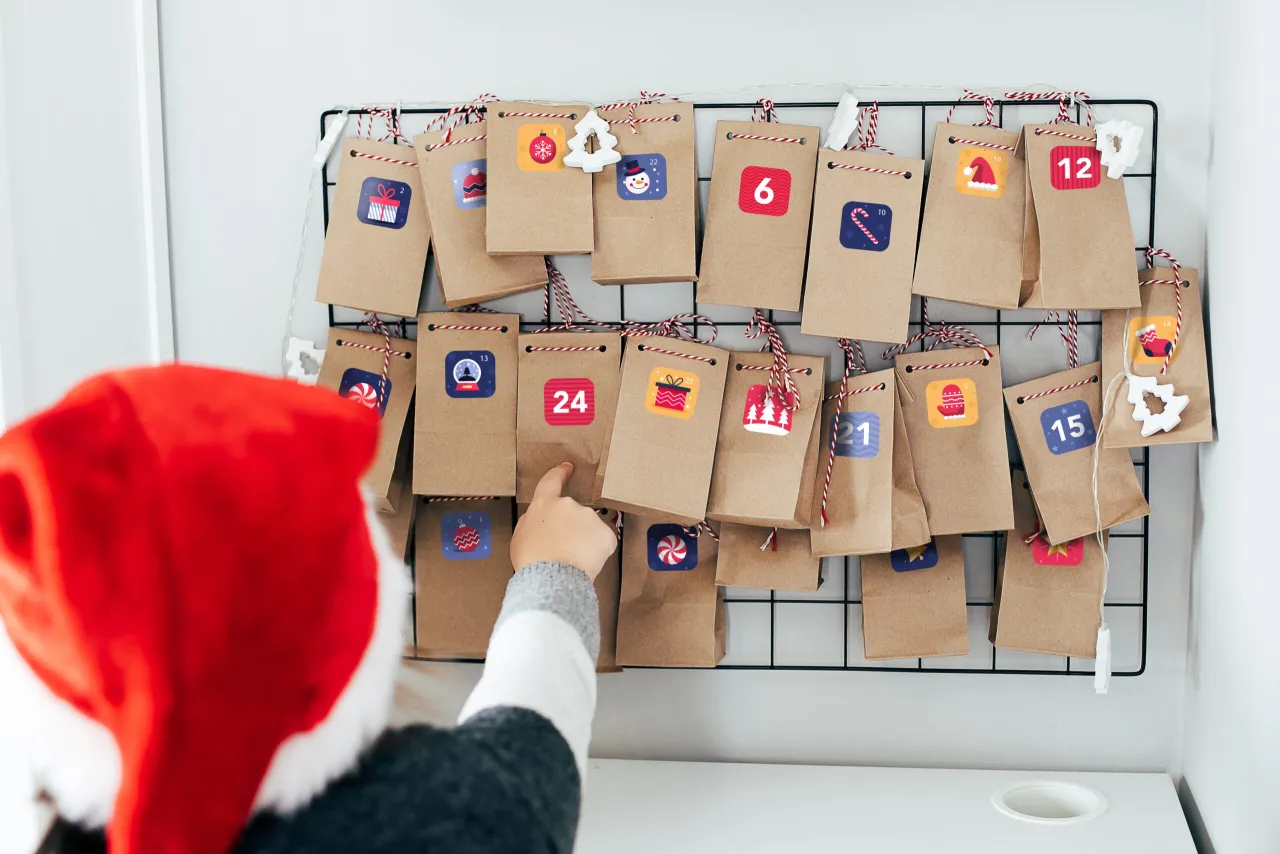 Dziecko w czapce Mikołaja wybiera prezent z kartonowego kalendarza adwentowego. Dowiedz się, jak zrobić kalendarz adwentowy z kartonu.