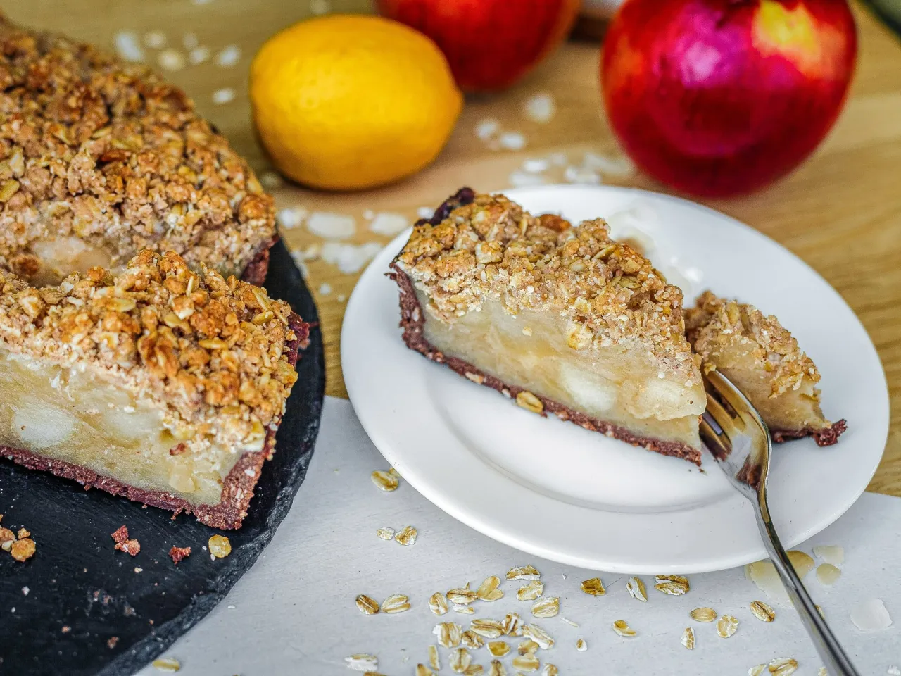 Kawałek szarlotki z kruszonką na talerzyku, obok jabłka i cytryna. Czy szarlotka jest zdrowa? Zależy od składników!