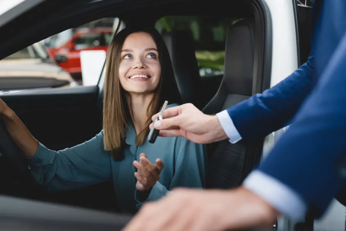 Uśmiechnięta kobieta odbiera kluczyki do samochodu, symbolizując wycofanie pojazdu z firmy i jego darowiznę.