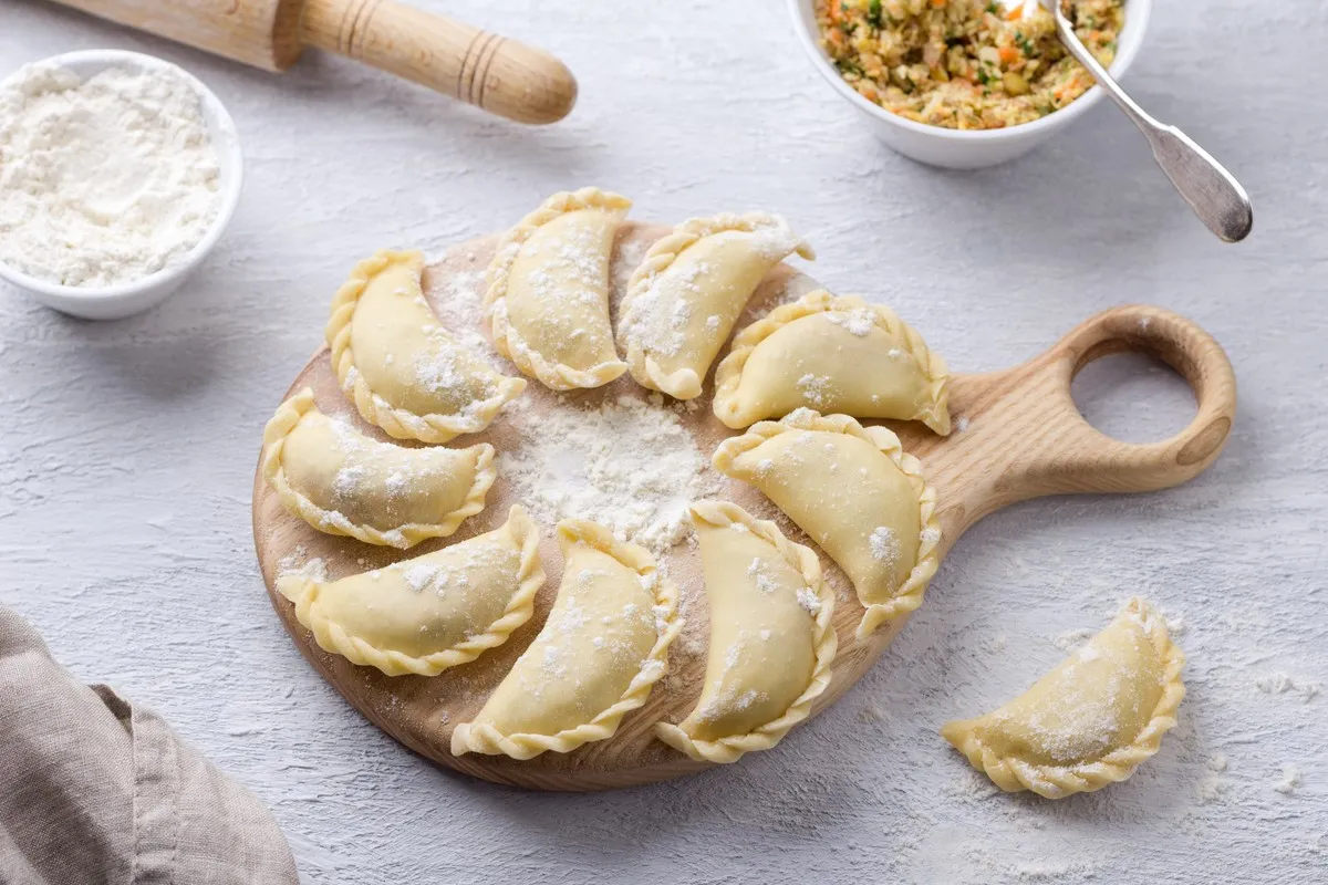 Surowe pierogi ułożone na desce. Czy ciasto na pierogi można zrobić dzień wcześniej? Tak, można je przechowywać w lod&oacute;wce.