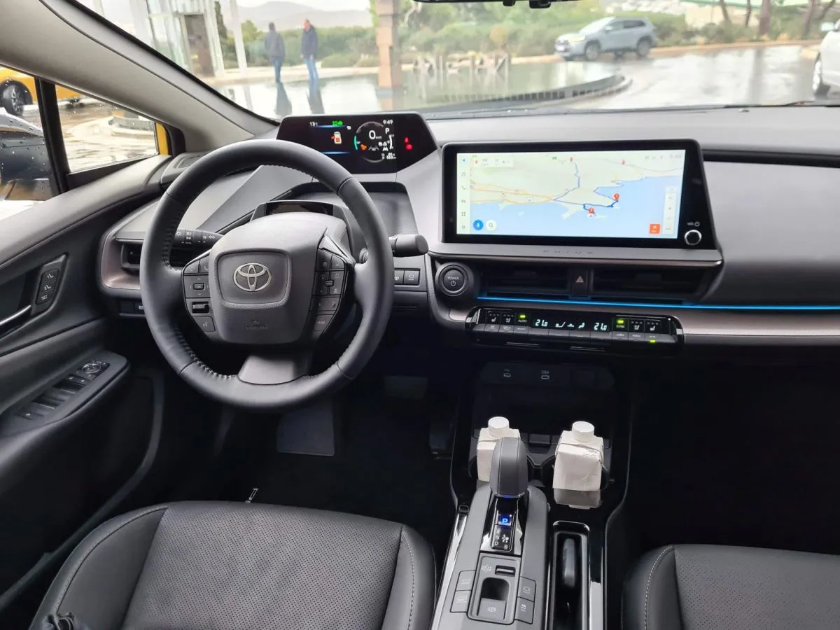 Wnętrze nowego Priusa. Czy warto kupić ten model? Nowoczesny kokpit z ekranem nawigacji i cyfrowymi zegarami.