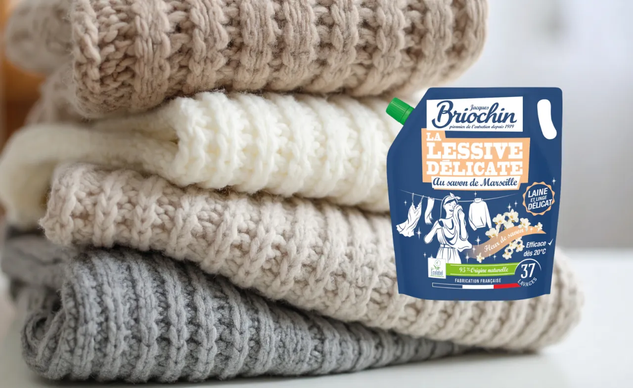 Stos delikatnych swetrów obok płynu do prania. Dowiedz się, jak prać swetry, by zachować ich miękkość.