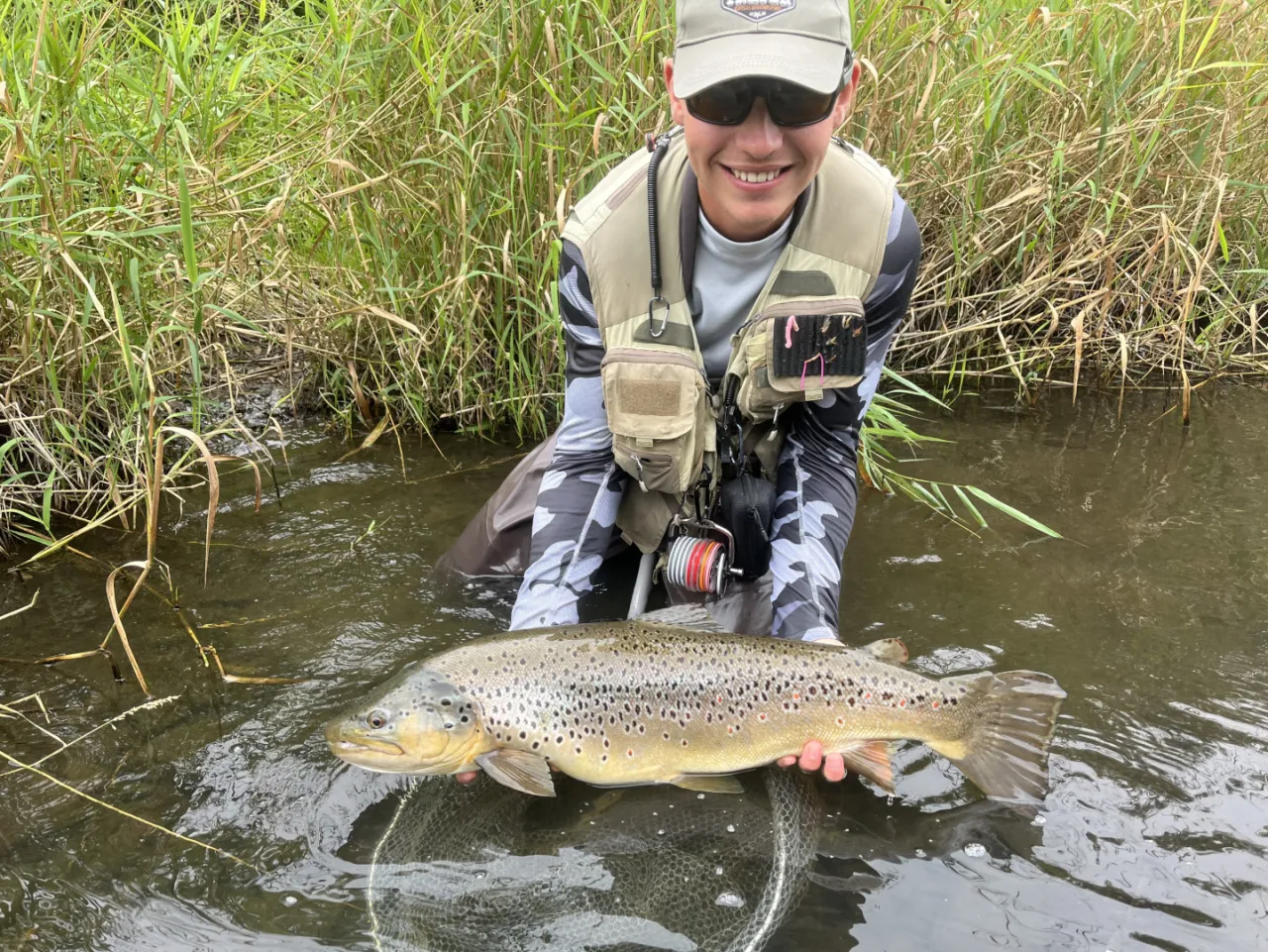 Szczęśliwy wędkarz trzyma w wodzie pięknego pstrąga. To dow&oacute;d, jaka wędka na pstrąga sprawdziła się najlepiej!