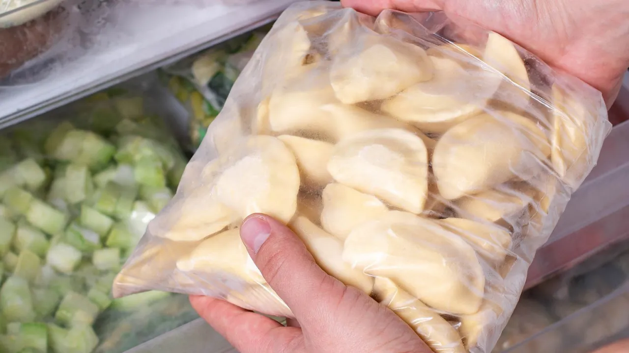 Ręce trzymają worek z pierogami, gotowe do zamrożenia. To świetny spos&oacute;b, jak pakować pierogi pr&oacute;żniowo, by zachowały świeżość.