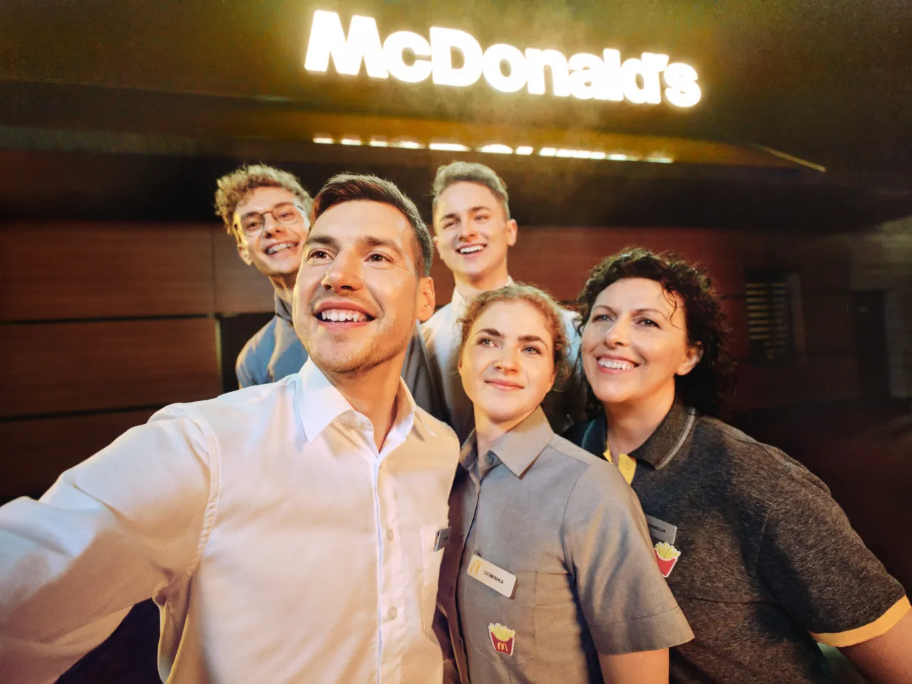 Uśmiechnięty zespół McDonald's przed neonowym logo. Zastanawiasz się, ile zarabia pracownik McDonald's?
