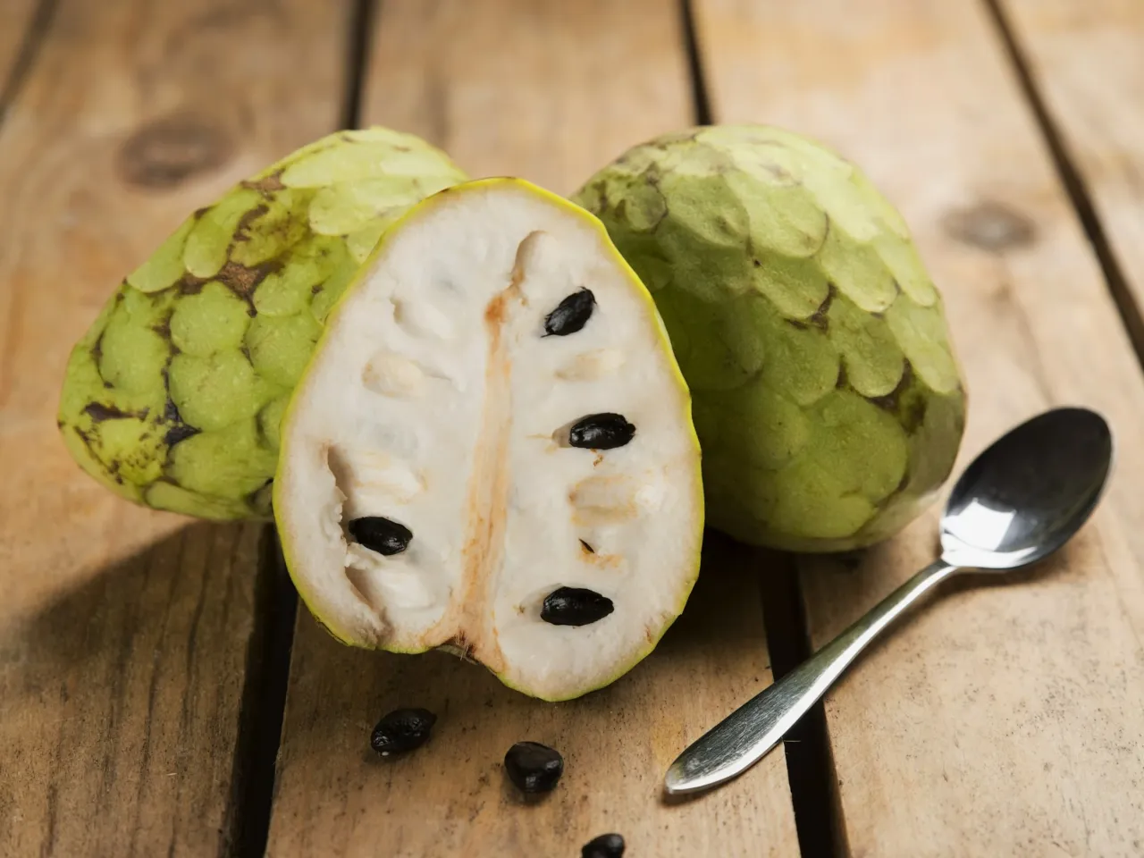 Dwa całe i przekrojone na p&oacute;ł cherimoya z czarnymi pestkami, gotowe do spr&oacute;bowania. Ich słodki, tropikalny smak zachwyca.