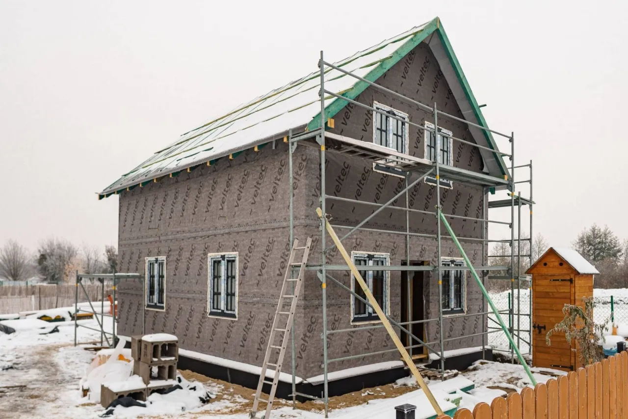 Budowa domu szkieletowego zimą. Rusztowania otaczają budynek, a na dachu widać śnieg. Pytanie 