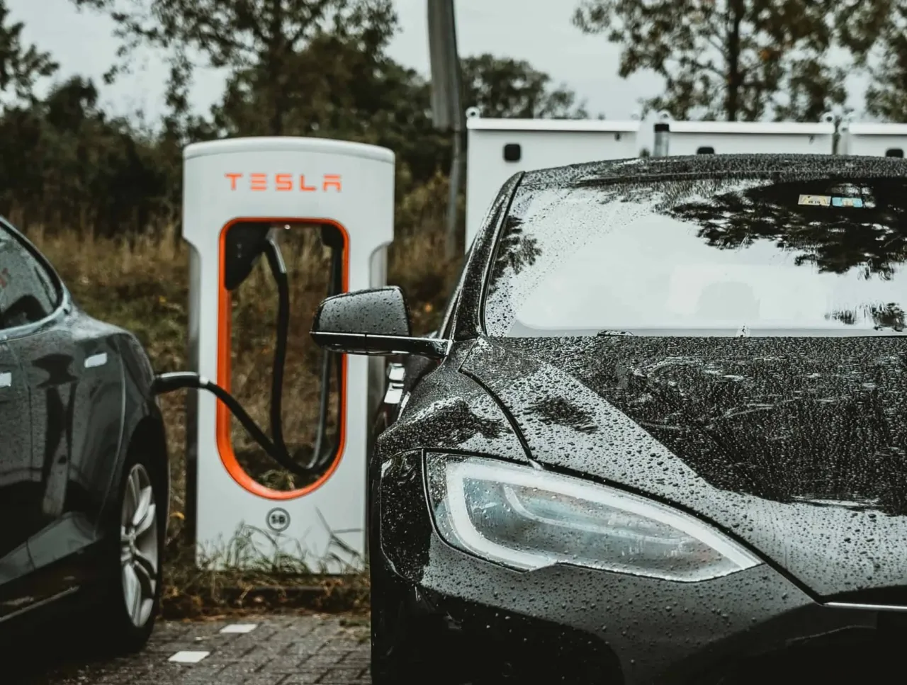 Czarna Tesla na deszczu pod ładowarką. Zastanawiasz się, ile trwa ładowanie Tesli? Czas zależy od modelu i mocy ładowarki.