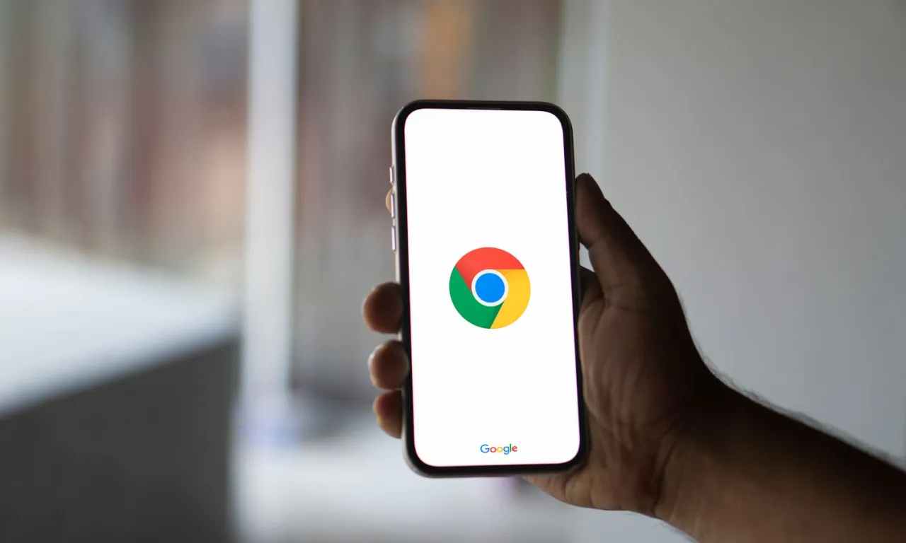 Dłoń trzyma smartfon z logo Chrome. Dowiedz się, jak zaktualizować przeglądarkę w telefonie, by cieszyć się nowymi funkcjami.
