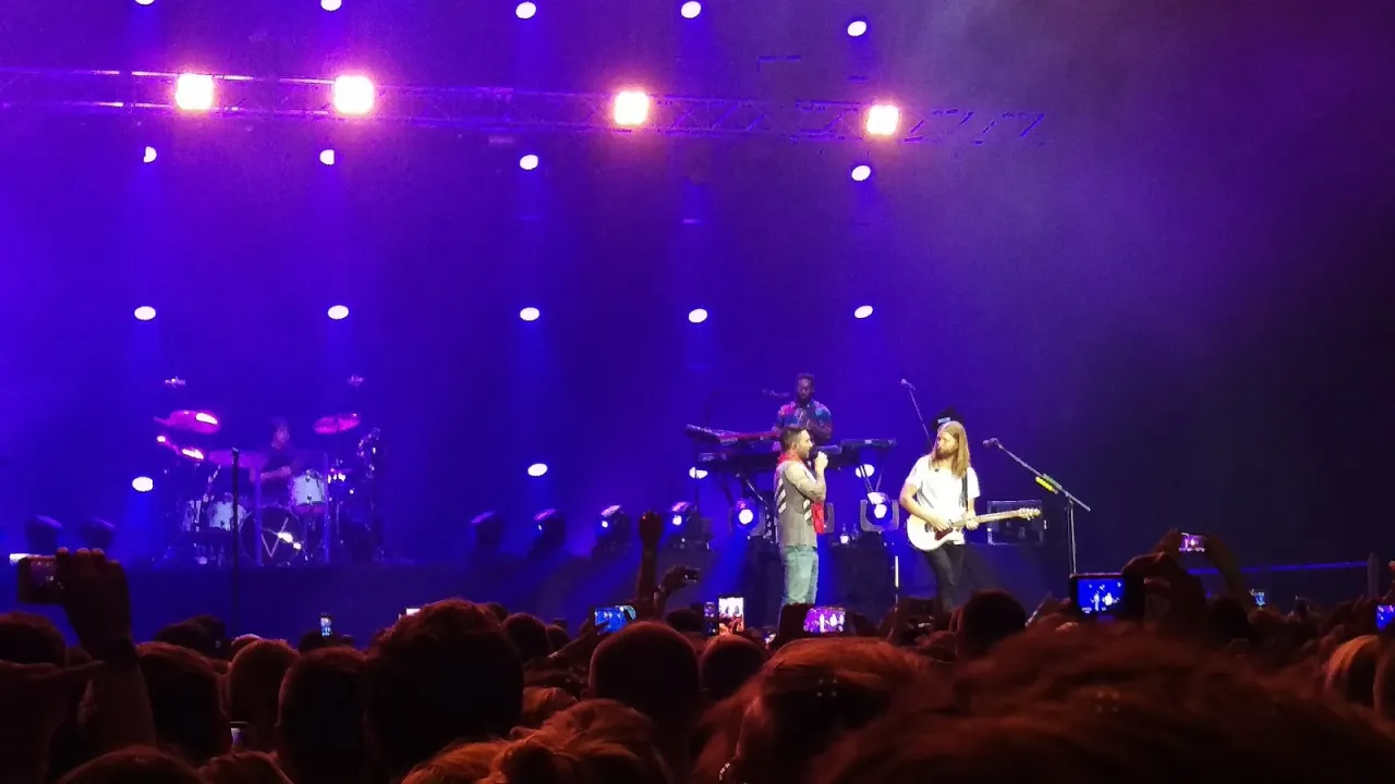 Koncert Maroon 5 w pełnym blasku fioletowych świateł. Fani nagrywają występ, zastanawiając się, ile trwa koncert Maroon 5.