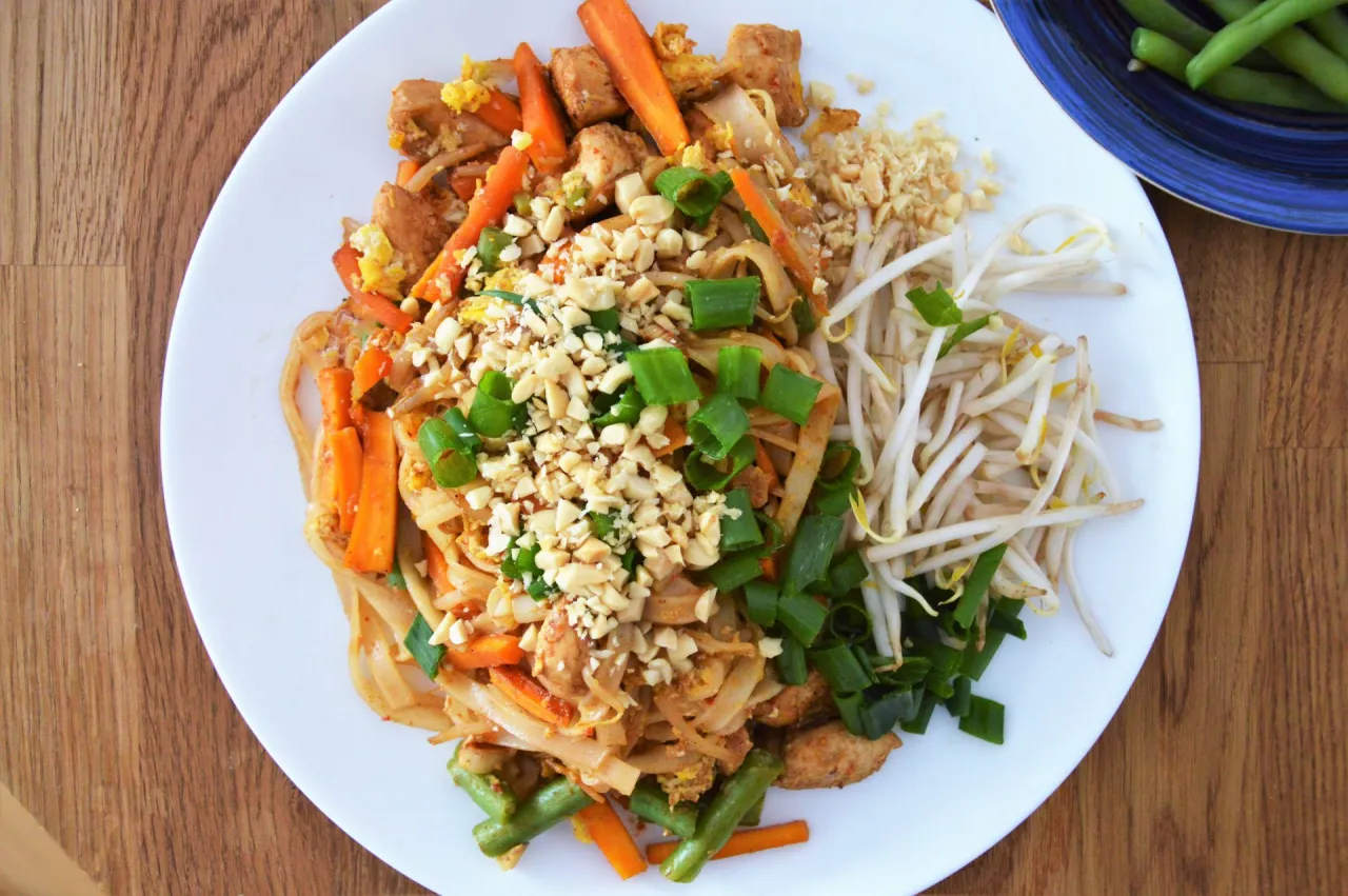 Pyszne pad thai skladniki: makaron ryżowy, kurczak, marchewka, fasolka szparagowa, kiełki fasoli mung, szczypiorek i posiekane orzeszki ziemne.