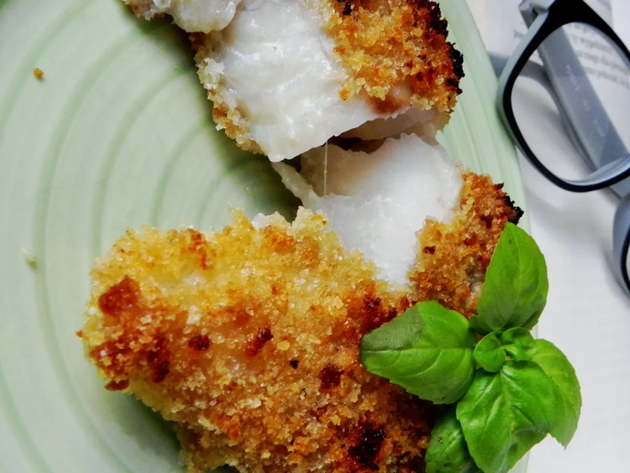 Chrupiąca ryba w panko, podana na zielonym talerzu, ozdobiona listkami bazylii.
