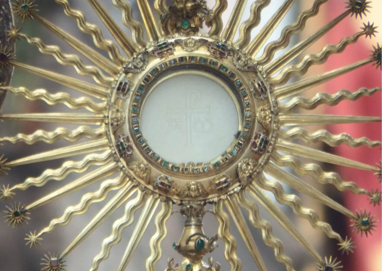 Złota monstrancja z hostią, symbolizująca wystawienie Najświętszego Sakramentu, ozdobiona klejnotami i promieniami.