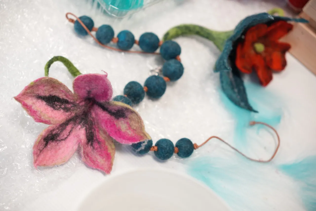 R&oacute;żowa i czerwona biżuteria z filcu w kształcie kwiat&oacute;w, połączona z niebieskimi koralikami.