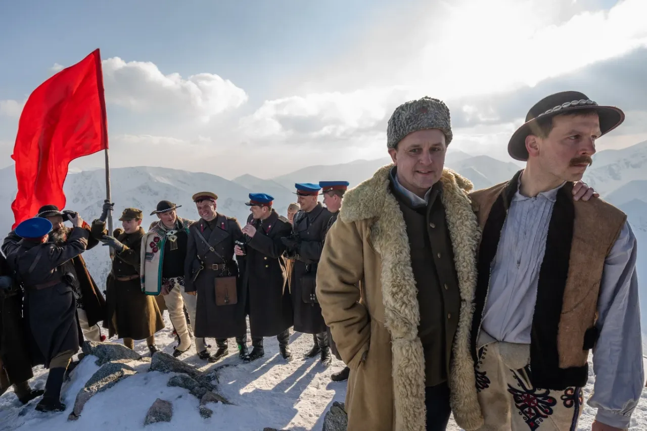 Grupa mężczyzn w historycznych strojach, z czerwoną flagą na szczycie góry. Recenzja