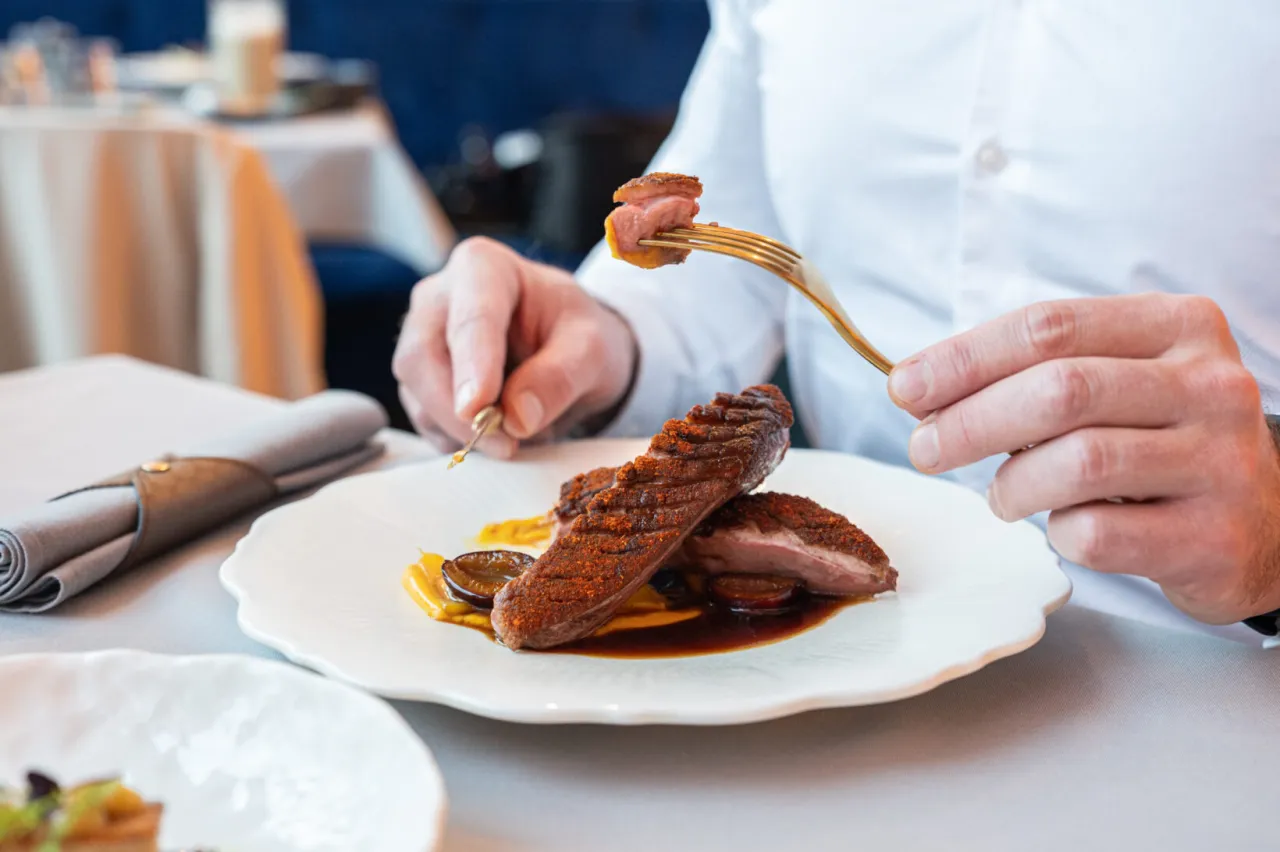 Eleganckie danie z kaczki na talerzu, idealne jako przepis na obiad jak z restauracji. Złoty widelec podnosi kawałek mięsa.