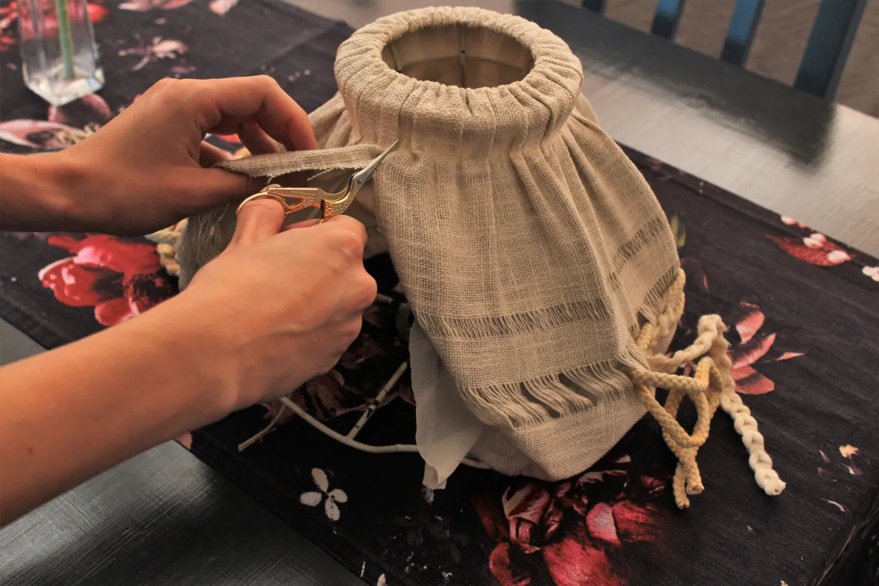 Ręce przycinają materiał, by zrobić abażur ze sznurka jutowego. Widać fragmenty sznurka i ozdobny materiał.