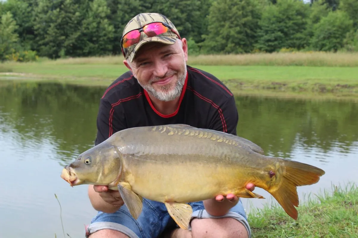 Szczęśliwy wędkarz z karpiem, kt&oacute;ry złowił na chleb. Pokazuje, jak założyć chleb na haczyk, by złapać taką rybę.