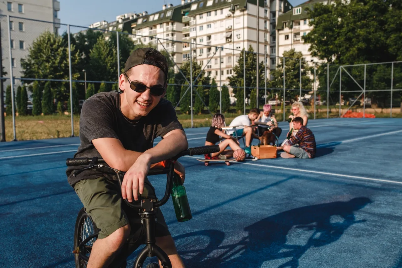 Chłopak na rowerze z butelką piwa, obok grupa znajomych. Czy można stracić prawo jazdy jadąc rowerem?