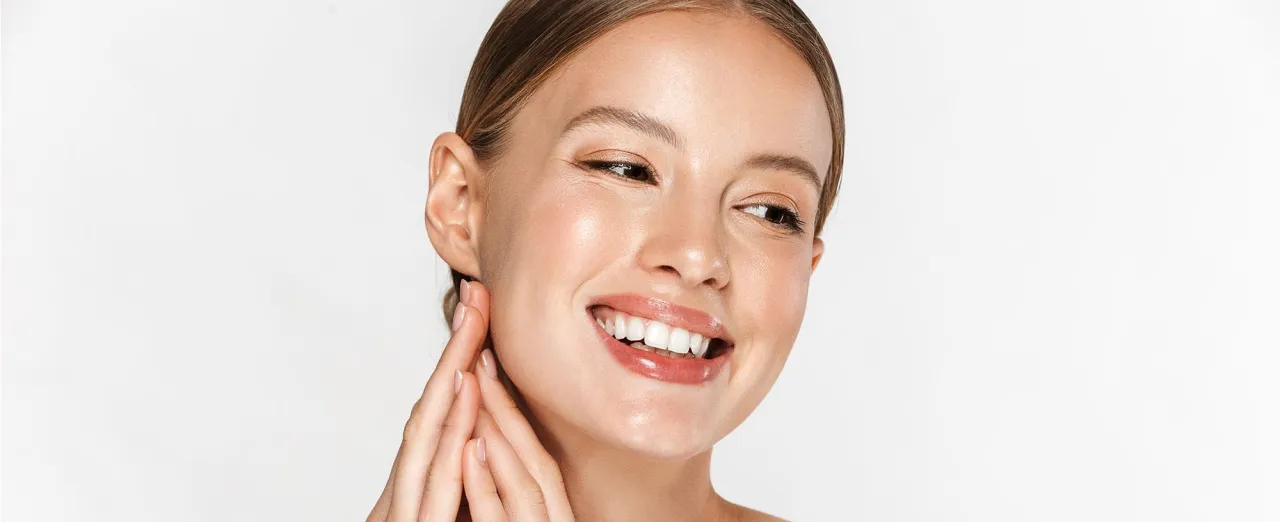 Uśmiechnięta twarz kobiety z promienną cerą, muśniętą pudrem rozświetlającym na całą twarz.