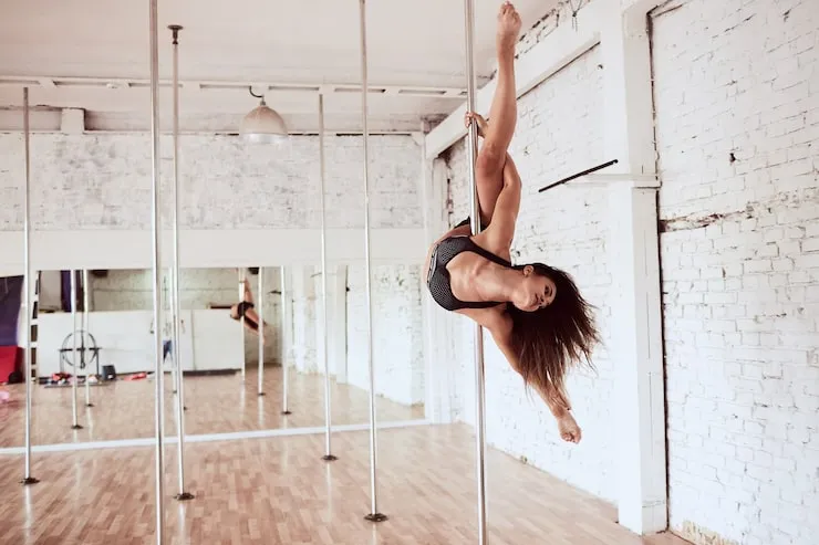 szczęśliwa kobieta wykonująca figurę na rurze pole dance