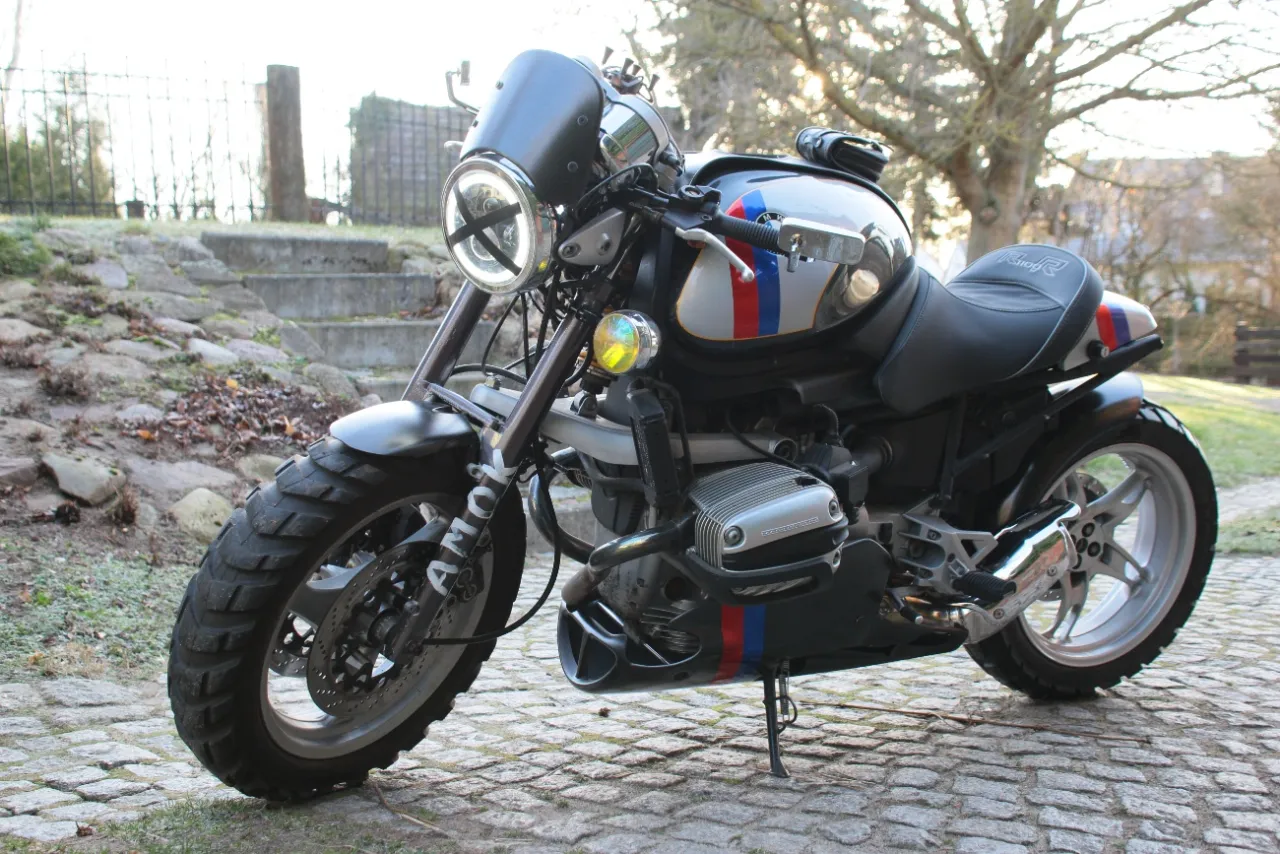 Zmodyfikowany BMW R 1100 R z charakterystycznymi pasami, gotowy na przygodę.