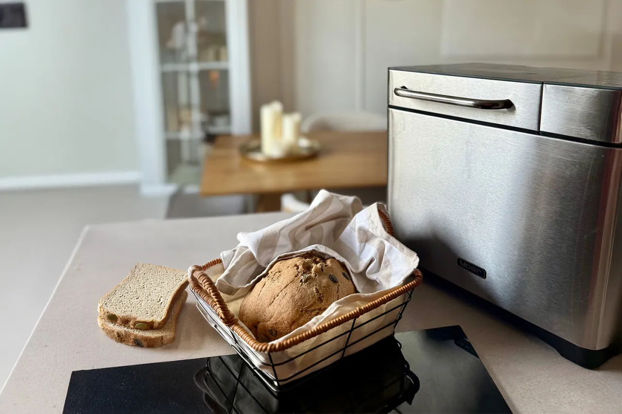 Świeżo upieczony chleb z maszyny, idealny na zdrowy posiłek. Obok kromki i koszyk z bochenkiem.