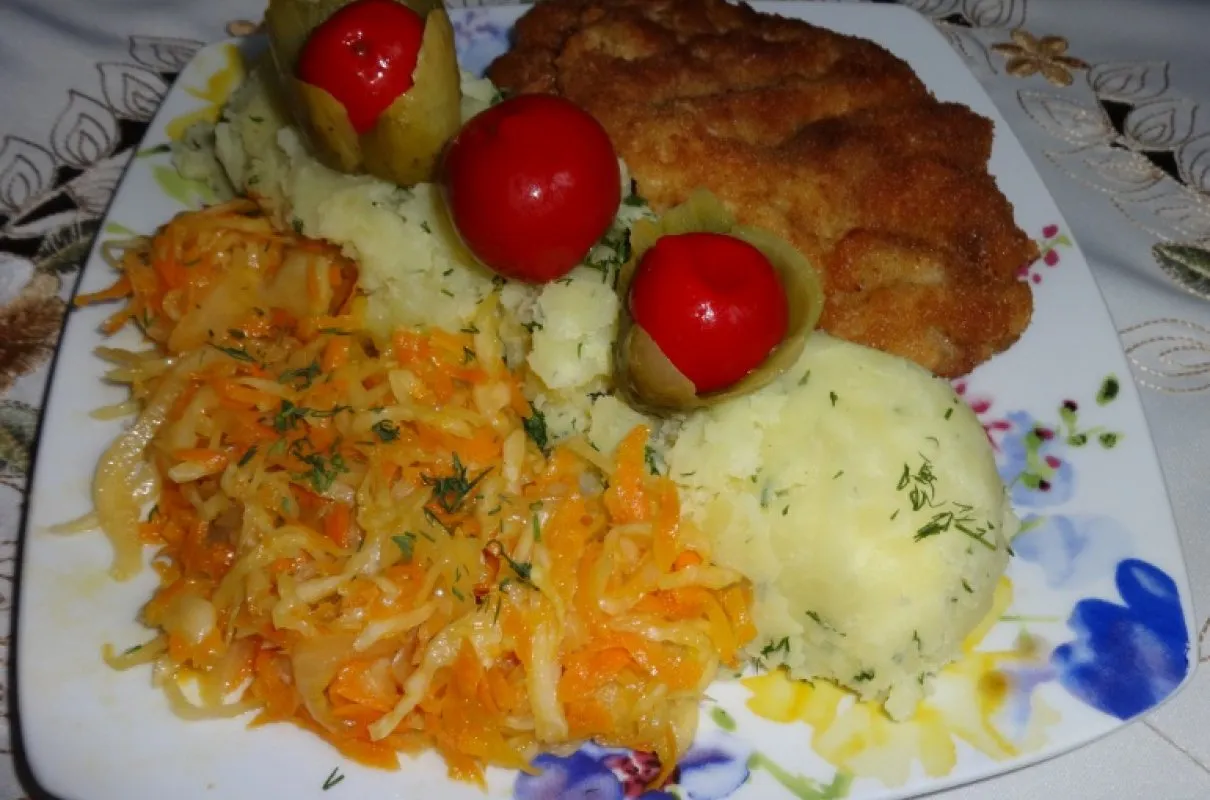 Talerz z kotletem schabowym, ziemniakami, surówką z marchewki i kapusty oraz marynowanymi pomidorkami. Idealne dodatki, co pasuje do schabowego!